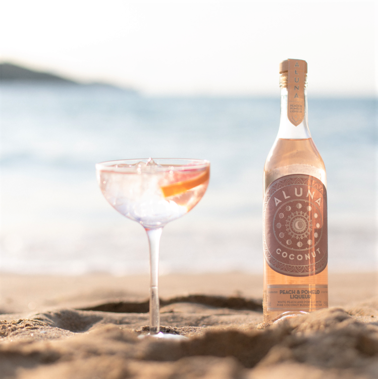 Aluna Peach &amp; Pomelo Bottle on beach.png